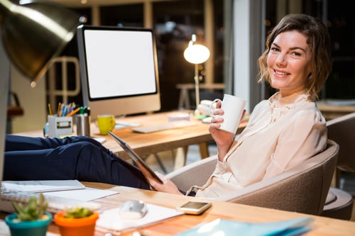 Portrait of businesswoman holding digital tablet and coffee cup at her desk in the office